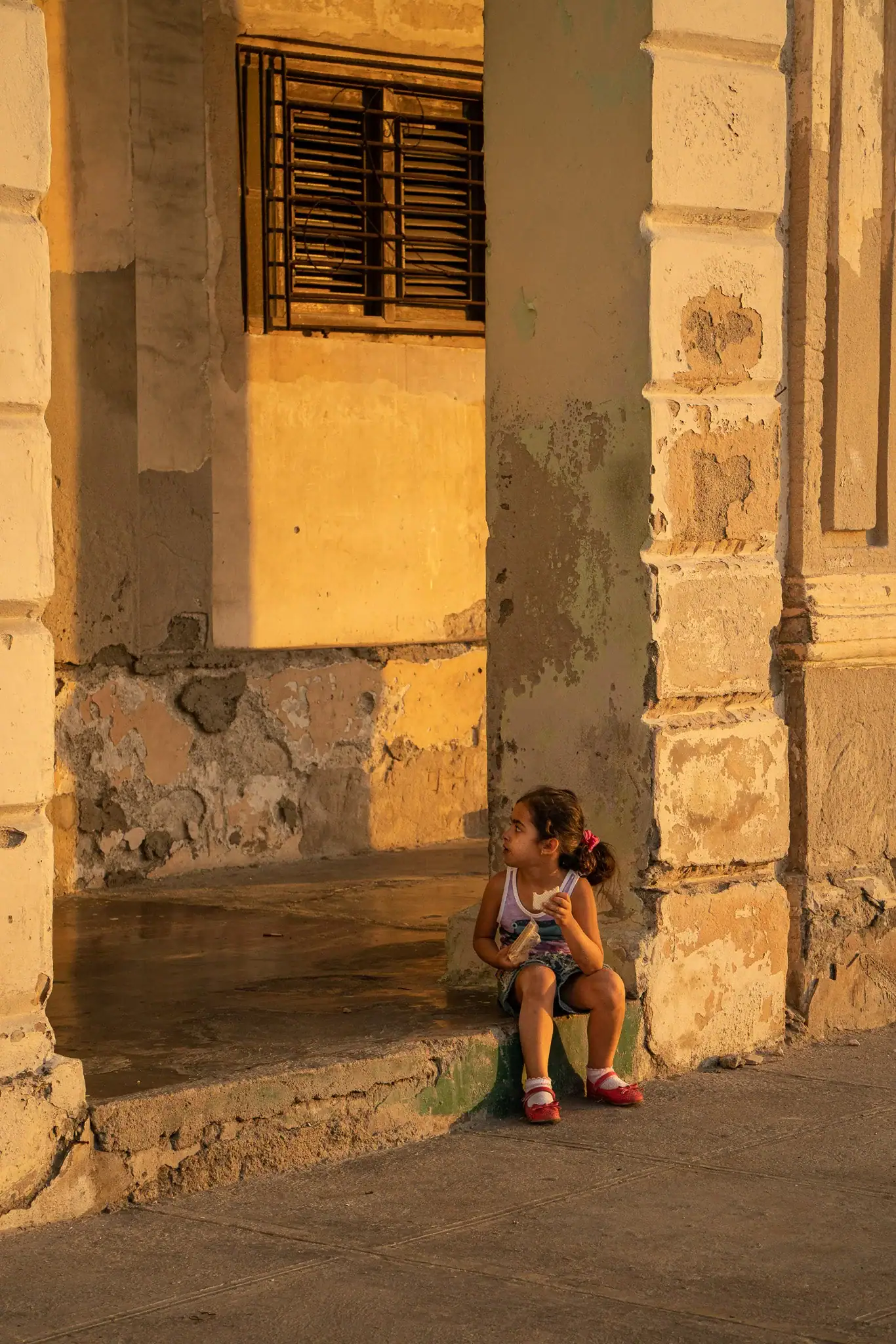 Young girl eating sandwich in Havana street lit by sunset