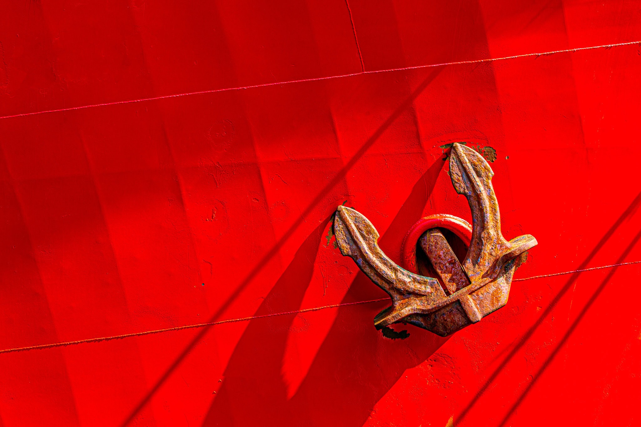 Rusted Ship Anchor Against Bright Red Hull – Industrial Wall Art