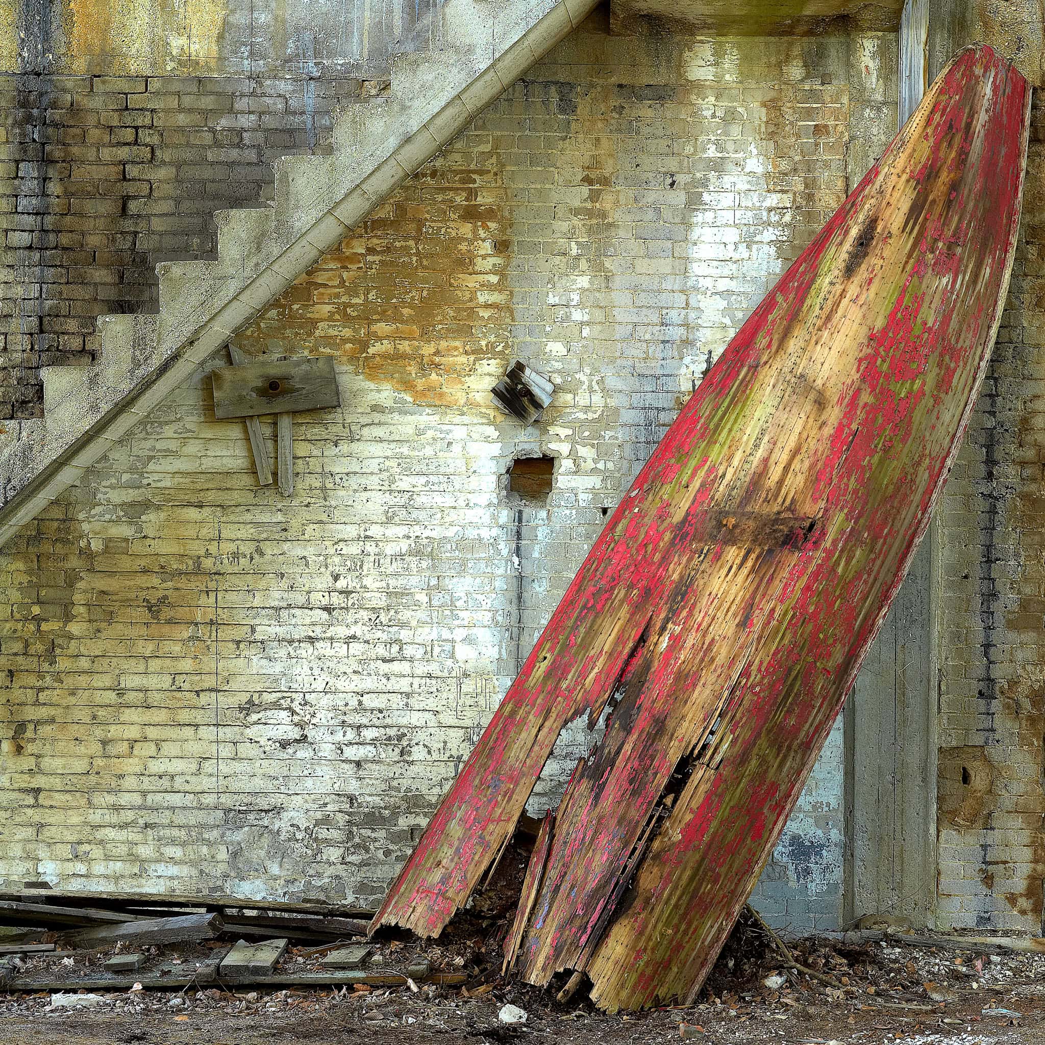 Red Rowboat Resting Against Aged Stone Wall – Fine Art Print