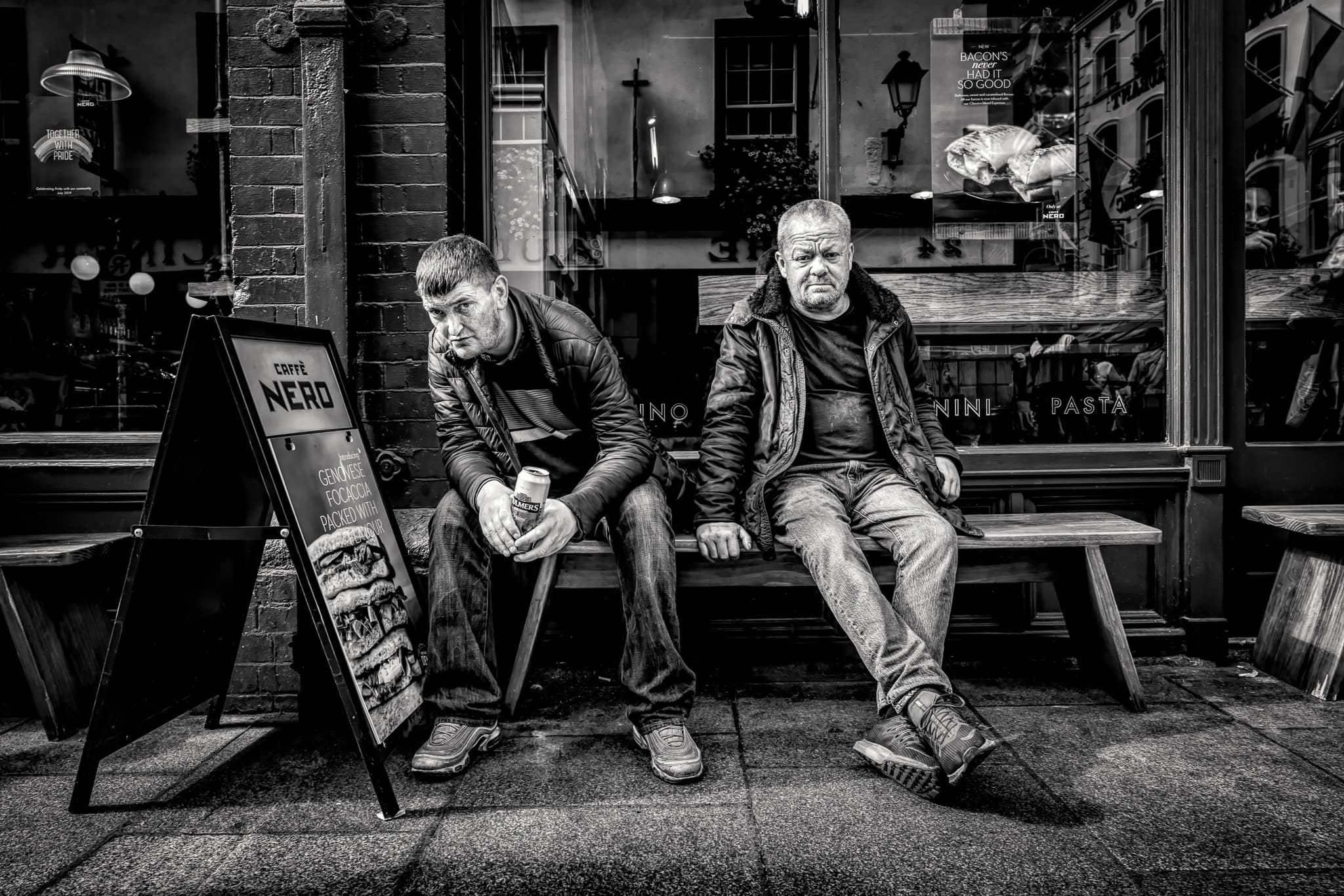 Two men sitting outside a Caffè Nero in Dublin, captured in high-contrast black and white street photography by Dan Kosmayer.