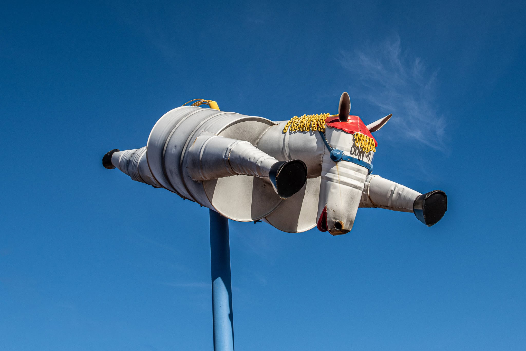 Flying tin horse sculpture made from metal barrels, suspended on a pole along Tin Horse Highway in Western Australia under a bright blue sky.