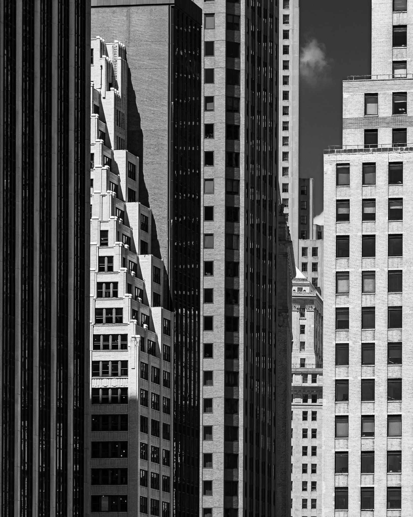 Black and white photo of densely packed skyscrapers in Manhattan, New York City, with sharp light and shadows defining architectural lines.